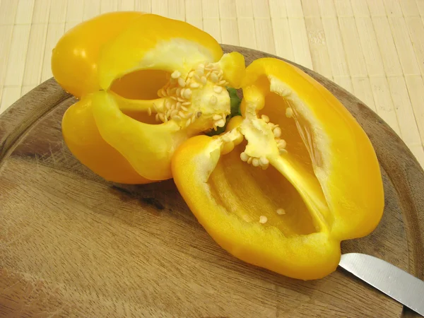 Halved yellow pepper on wooden plate with knife — Stock Photo, Image