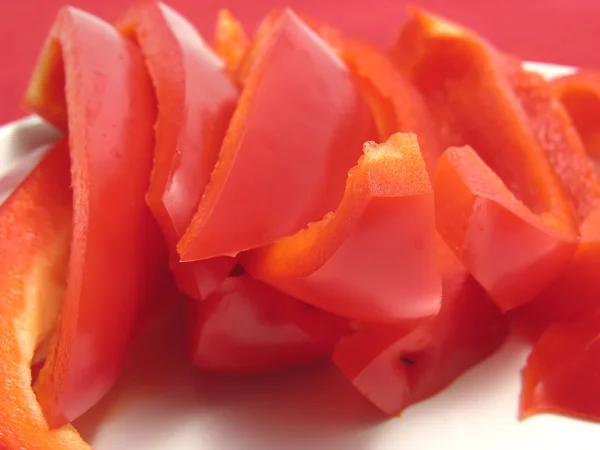 Poivron rouge tranché sur une assiette blanche et napperon rouge — Photo