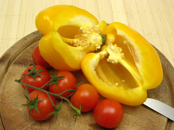 Halverade gul paprika och tomater på träplatta med kniv — Stockfoto