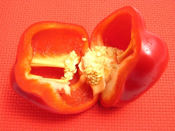 Rode paprika, gesneden in helften op een rode placemat — Stockfoto