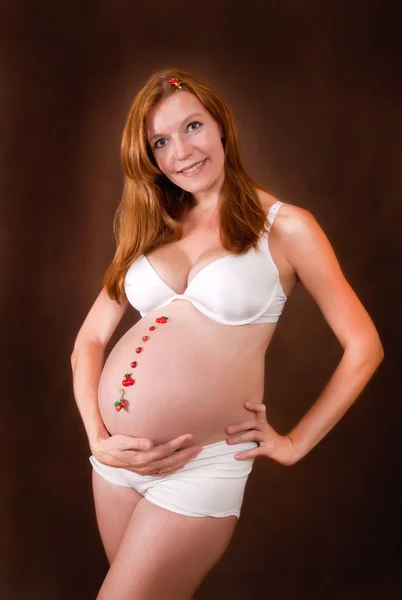 Zwangere jonge vrouw in witte kledingassortiment Stockfoto