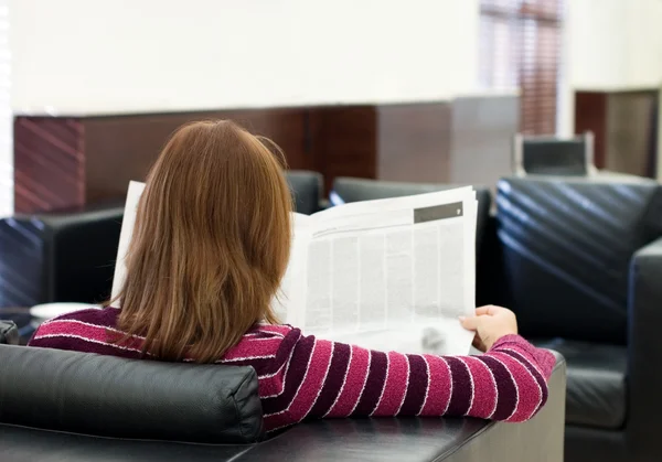 Het meisje leest de krant in een leunstoel — Stockfoto