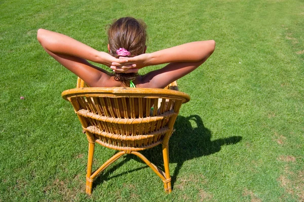 A menina senta-se em uma poltrona em uma grama — Fotografia de Stock