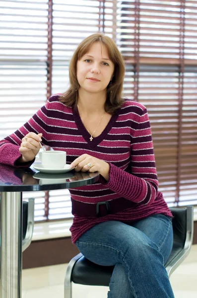 Dívka pije kávu za stolem v kavárně — Stock fotografie