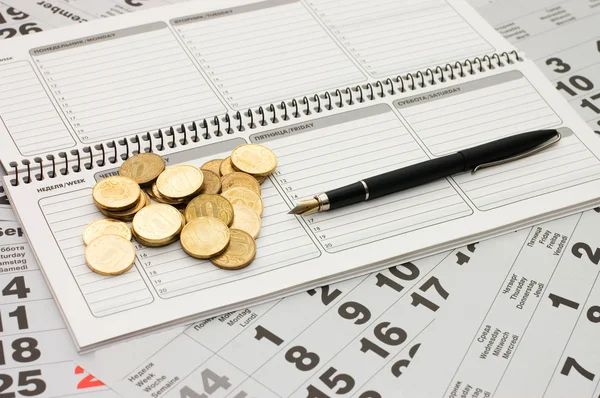 Fogli di un calendario con monete e un notebook — Foto Stock