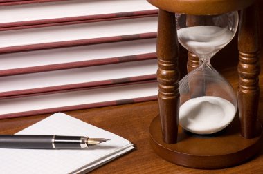 Hourglasses and book on a wooden table clipart