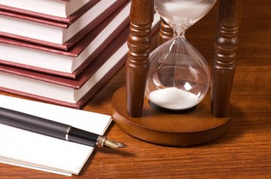 Hourglasses and book on a wooden table clipart