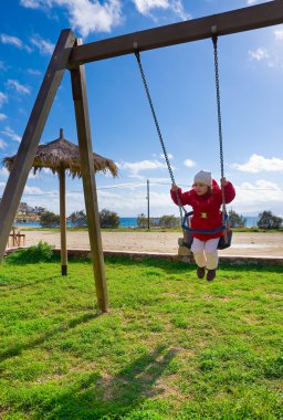 The little girl on a swing against the sea and sky clipart