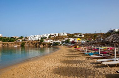 Sandy beach on the island of Mykonos with umbrellas and color sun beds clipart