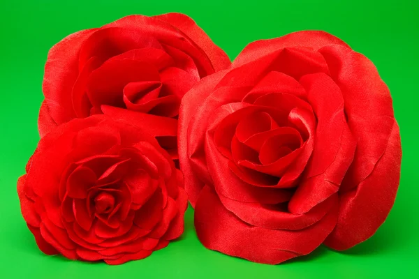 在绿色背景上三个装饰红丝绸玫瑰 — 图库照片