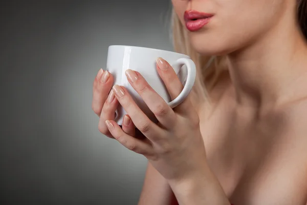 Kvinnan håller varm kopp och blåser på den — Stockfoto