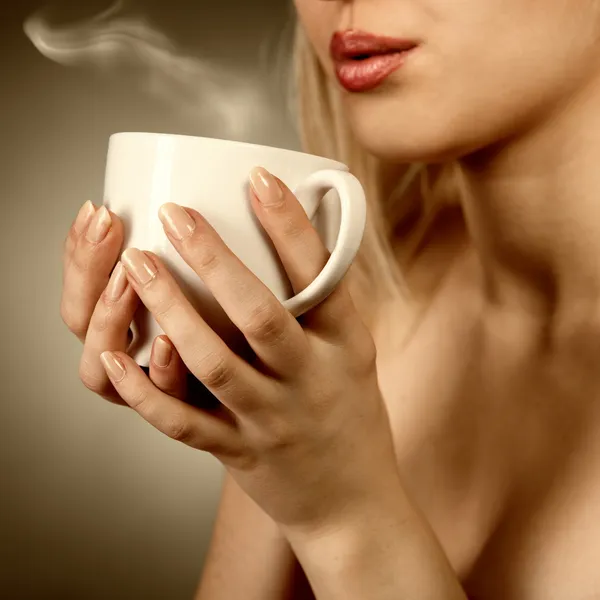 Woman holding hot cup and blowing on it — Stock Photo, Image