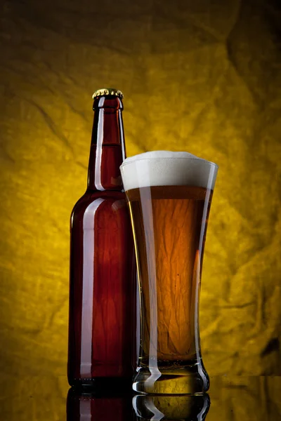 Öl i glaset med flaska på gul bakgrund — Stockfoto