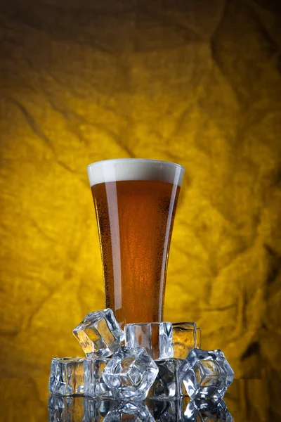 Beer in glass with ice cubes on yellow background — Stock Photo, Image