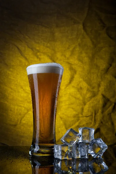 Cerveja em vidro com cubos de gelo sobre fundo amarelo — Fotografia de Stock