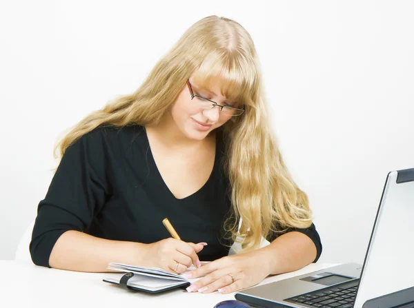 Девушка с ноутбуком пишет в блокноте — стоковое фото