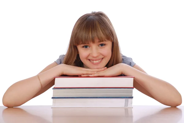 Dívka sedí u stolu a dát ruce na hromadě knih. — Stock fotografie