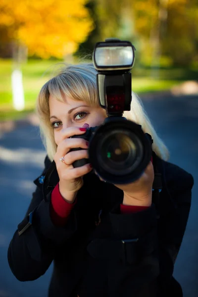 stock image A girl holds a professional camera. Smile looks out from behind the camera.