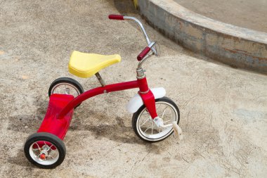 Abandoned red tricycle with a yellow seat sits on concrete pad. clipart