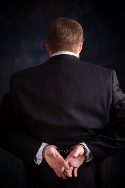 Businessman in suit is handcuffed behind his back. clipart