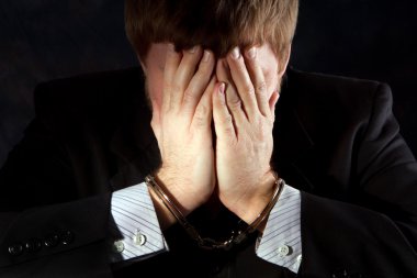 Handcuffs businessman covers his face to hid his identity from shame. clipart