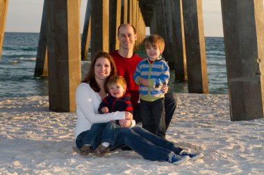 Young family poses for a beach portrait under a pier. clipart