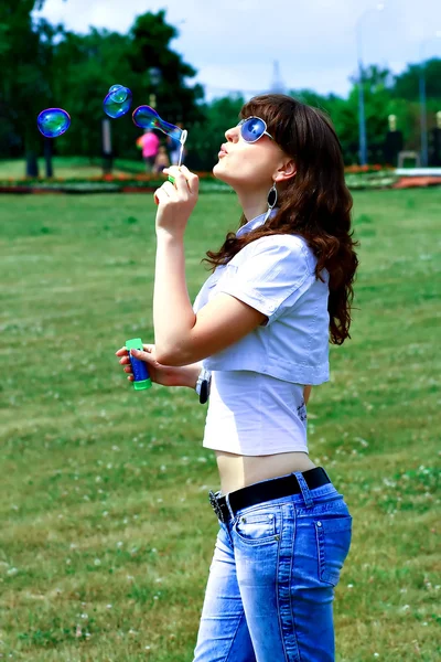 Молодая девушка надувает мыльные пузыри в осеннем парке — стоковое фото