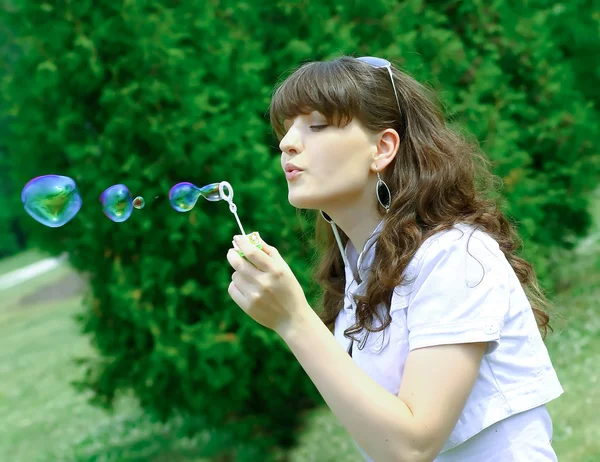 Молодая девушка надувает мыльные пузыри в осеннем парке — стоковое фото