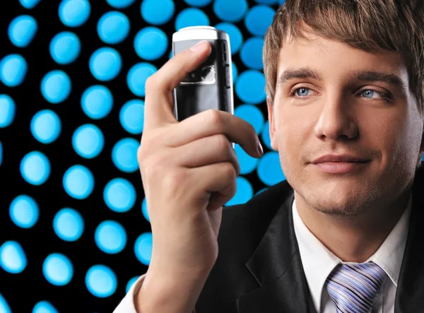 Молодой бизнесмен держит мобильный телефон на абстрактном фоне — стоковое фото