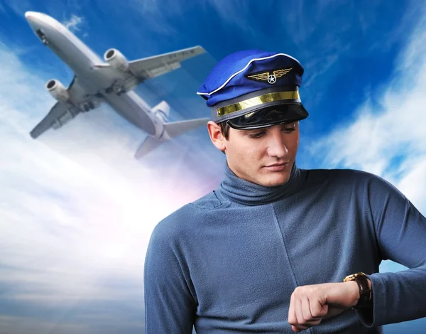 Knappe piloot tegen blauwe hemel en vliegende vliegtuig — Stockfoto