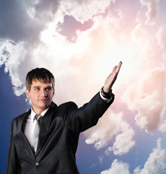 Knappe jonge zakenman met uitgestrekte hand tegen bewolkte hemel — Stockfoto
