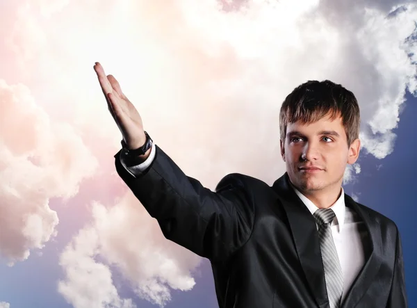 Knappe jonge zakenman met uitgestrekte hand tegen bewolkte hemel — Stockfoto