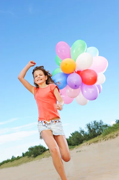 Счастливая девушка с воздушными шариками, бегущими по пляжу — стоковое фото