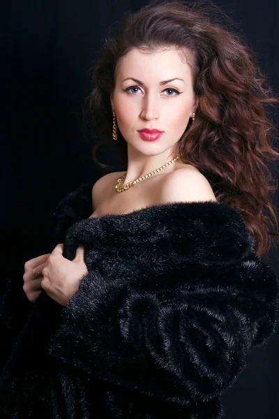 Krásná mladá žena v černém kožichu a šperky — Stock fotografie