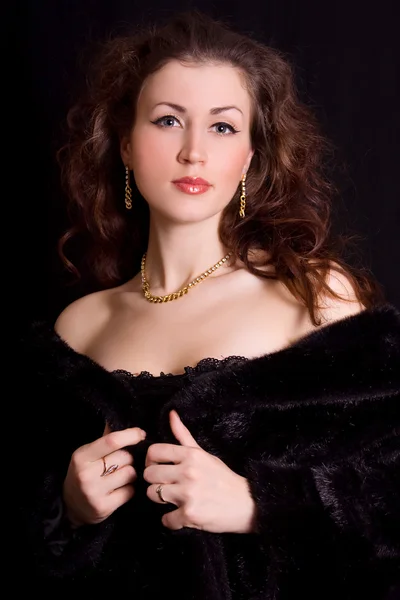 Beautiful young woman in a black fur coat and jewelry — Stock Photo, Image