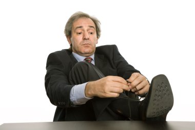 Mature business man tying his shoe in a desk clipart