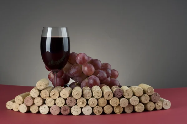 Red wine glass with grape and corks. — Stock Photo, Image