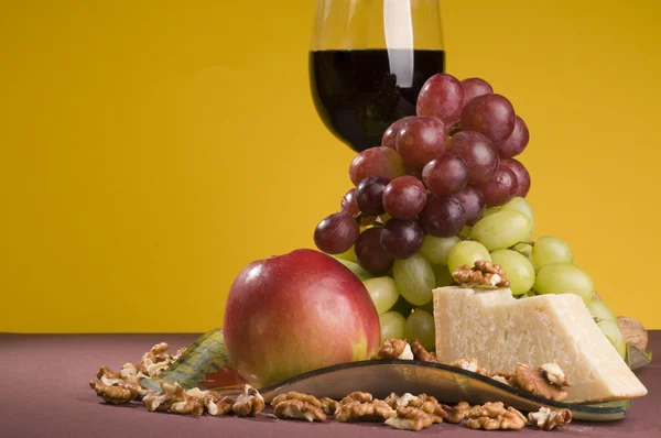 Vinho tinto com uva, maçã e queijo em um prato . — Fotografia de Stock