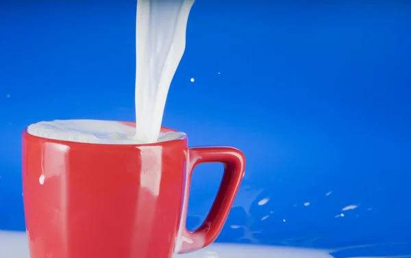 Pouring milk into a red cup — Stock Photo, Image