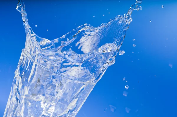 Свіжа вода виливається зі склянки над синім — стокове фото