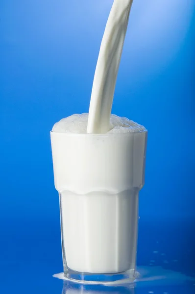 Derramando leite sobre fundo azul — Fotografia de Stock