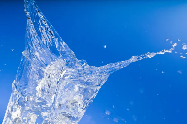 Água doce salpicando de um copo sobre azul — Fotografia de Stock