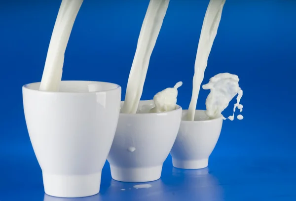 Milch über blauen Hintergrund gießen — Stockfoto