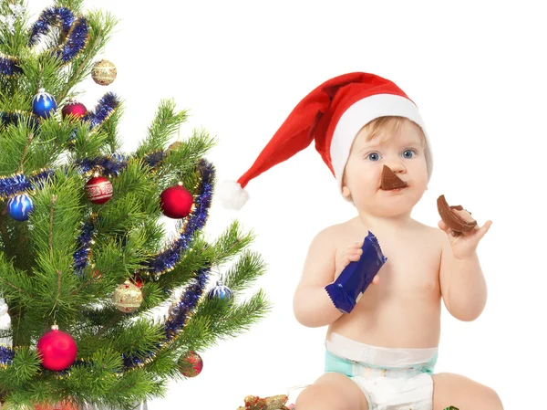 Niedliches kleines Mädchen in der Nähe des Weihnachtsbaums isst Schokoladenei isolat — Stockfoto