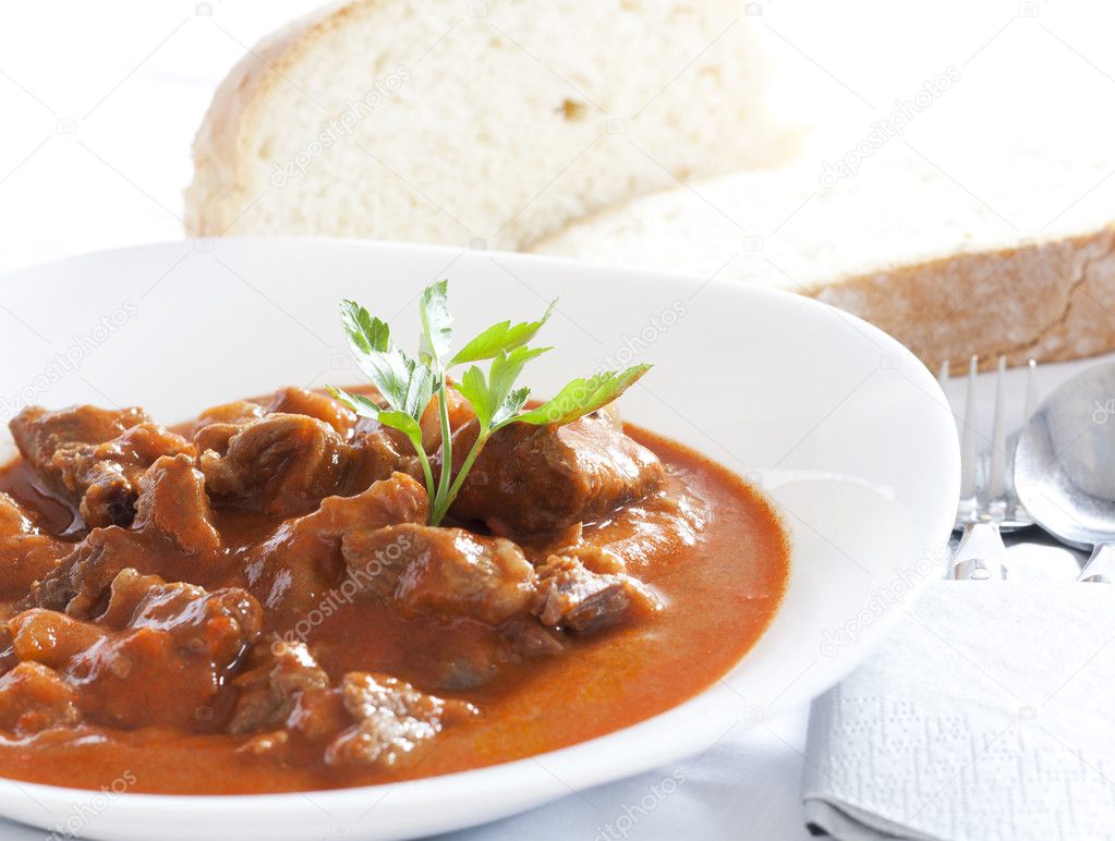 Goulash stew served in white bowl. Bread in the background