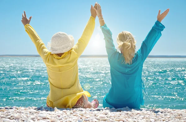 Girls with arms raised sitting on beach — Stock Photo, Image
