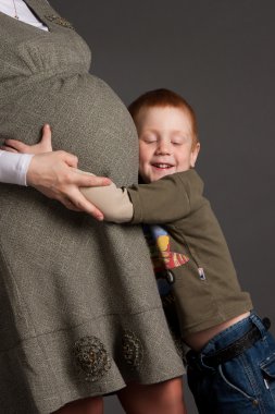 Little boy gently embrace pregnant mother, studio shoot clipart