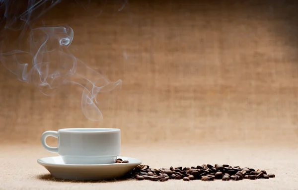 Xícara de café quente sobre a balsa e grãos de café no grunge — Fotografia de Stock