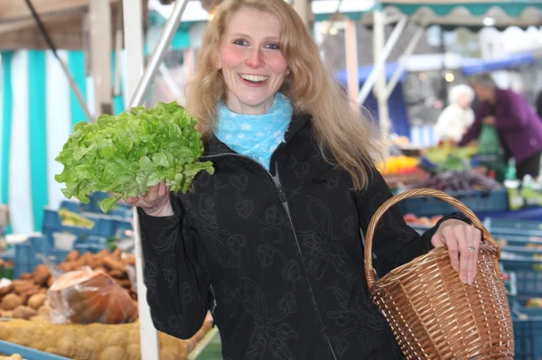 Une femme souriante au marché achète une salade fraîche — Photo