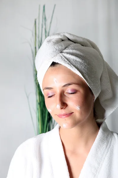 Mujer joven con toalla en la cabeza y crema en la piel — Foto de Stock